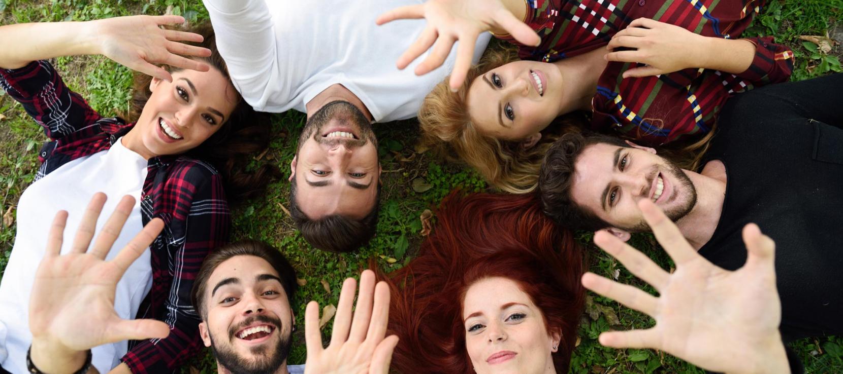Plusieurs étudiants couchés sur l'herbe tendent leur main vers le ciel Plusieurs étudiants couchés sur l'herbe tendent leur main vers le ciel